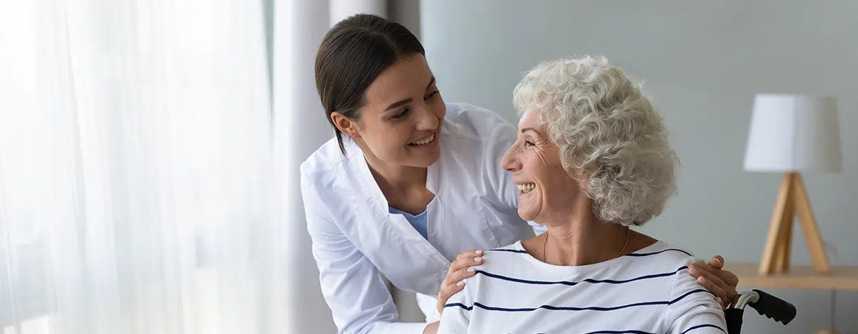 Smiling disabled elderly woman in wheelchair talking with caring nurse