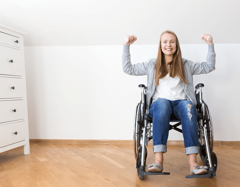 woman seated in wheelchair holding dumbbells above head