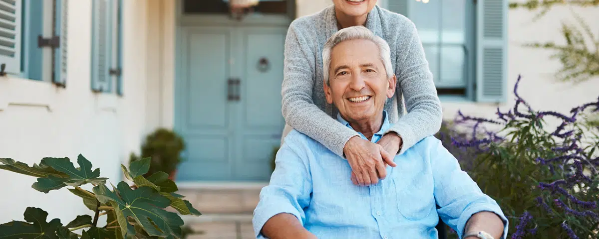 cheerful wheelchair bound senior man relaxing with his wife in their backyard at home