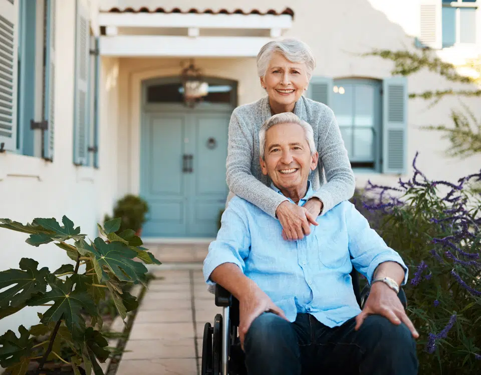 cheerful wheelchair bound senior man relaxing with his wife in their backyard at home