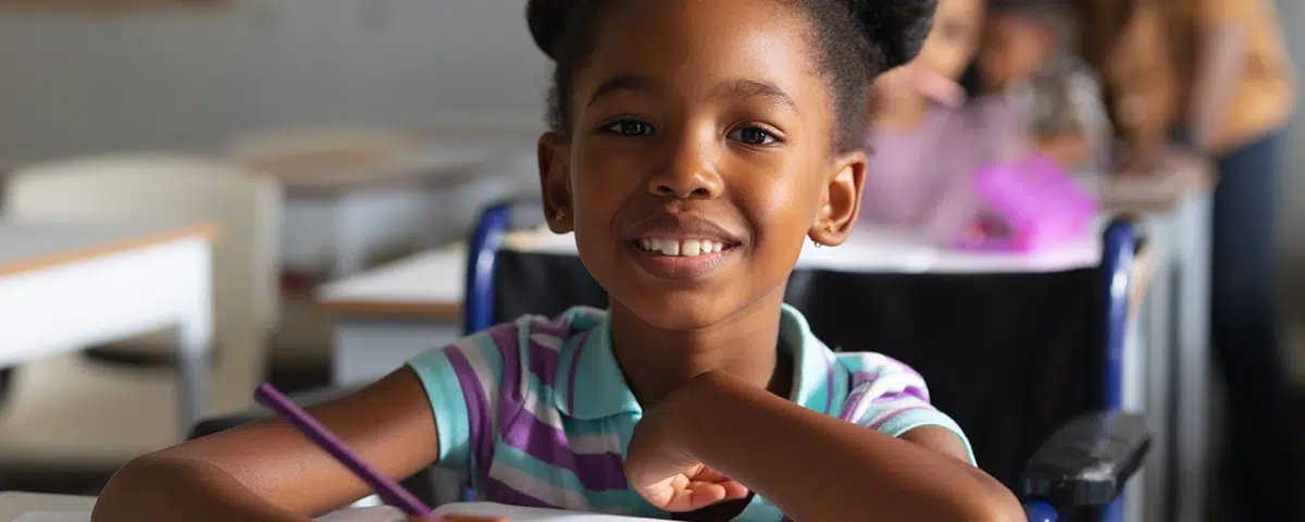 Portrait of smiling elementary girl studying while sitting on wheelchair at desk