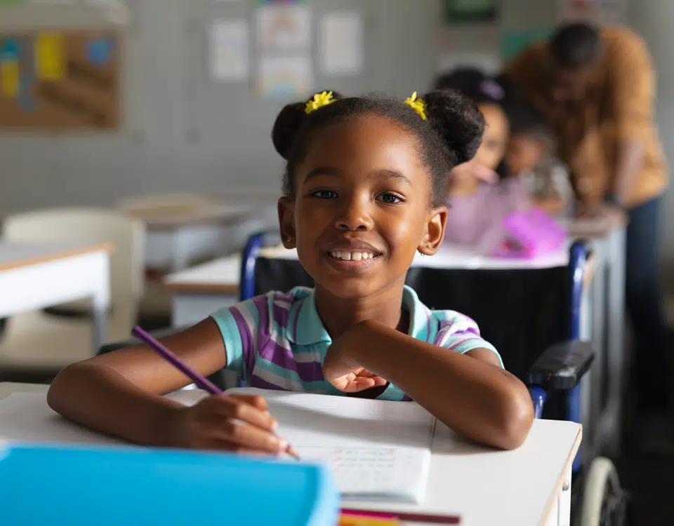 Portrait of smiling elementary girl studying while sitting on wheelchair at desk