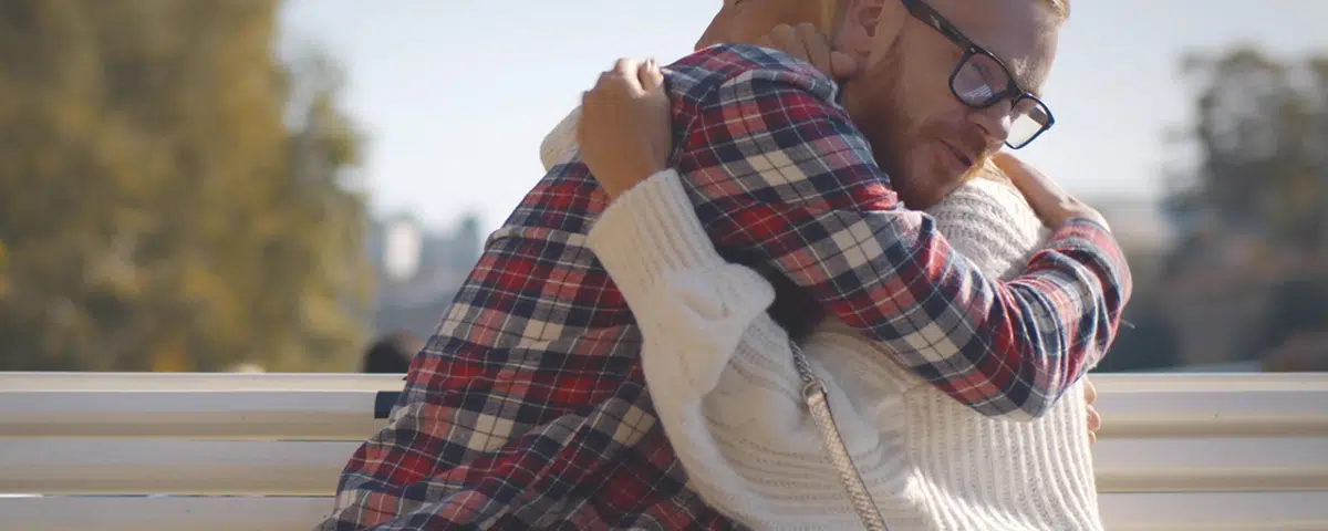 Senior woman and adult son hugging sitting together on bench in park