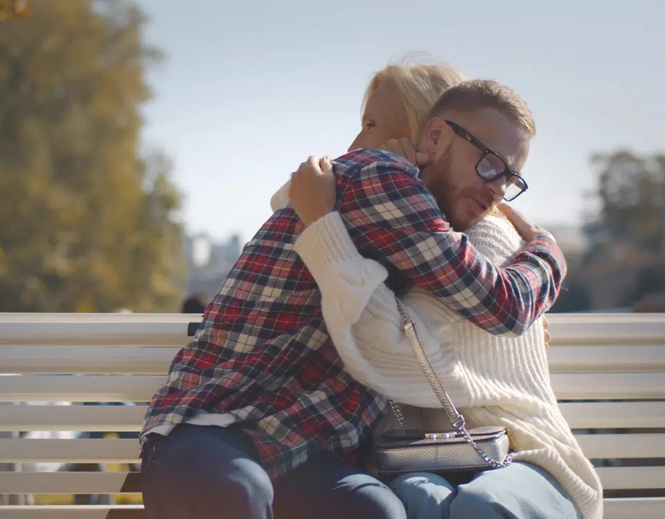 Senior woman and adult son hugging sitting together on bench in park